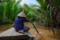 Vietnamese woman with typical hat rowing a wooden boat through water palms on Mekong Delta, Vietnam