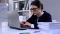 Woman typing on laptop, pile of documents lying on table, overload of work