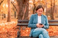 Woman typing text on mobile phone on autumn park bench Royalty Free Stock Photo