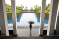 Woman with umbrella standing by swimming pool watching the rain Royalty Free Stock Photo