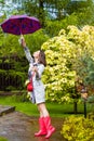 Woman with an umbrella, wearing red rubber boots and a raincoat in the rain in a blooming spring garden Royalty Free Stock Photo