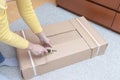 Woman unboxing a cardboard box with new furniture with construction knife - moving to new house and purchasing new furniture