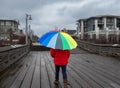 Woman under rainbow umbrella. Person walking with colorful umbrella on the pier at rainy day Royalty Free Stock Photo