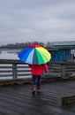 Woman under rainbow umbrella. Person walking with colorful umbrella on the pier at rainy day Royalty Free Stock Photo