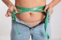 Woman in unfit jeans measuring her waist on light background, closeup. Weight loss concept Royalty Free Stock Photo