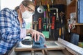 Mature Woman Upcycling Furniture In Workshop At Home Using Electric Sander Royalty Free Stock Photo