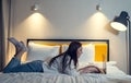 Woman use laptop on bed in evening. Lady lies on stomach and makes purchases in online stores or reads news and Royalty Free Stock Photo