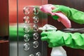 A woman uses a disinfectant spray and a wet wipe to clean the elevator button control panel Royalty Free Stock Photo