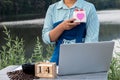 A woman uses a laptop and drinks coffee in nature with a gift box with a heart shape and a wooden calendar. The concept of love
