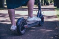 The woman uses a scooter. Women`s legs on an electric scooter on the track in the park