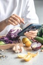 A woman uses a smartphone in the kitchen while preparing a vegetable salad.