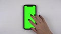 A woman uses a smartphone lying on the table. Green screen on phone. The girl taps her finger on the display. Hand close