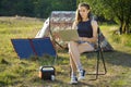 Woman uses solar panel to generate electricity for working on laptop outdoors Royalty Free Stock Photo