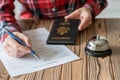 Woman using American passport filling hotel reservation form in the hotel. Silver vintage bell on wooden rustic reception desk. Royalty Free Stock Photo