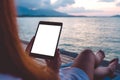 A woman using black tablet pc with blank white desktop screen while sitting by the sea with blue sky background Royalty Free Stock Photo