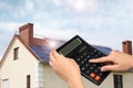 Woman using calculator against house with solar panels. Renewable energy and money saving Royalty Free Stock Photo