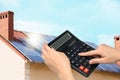 Woman using calculator against house with solar panels. Renewable energy and money saving Royalty Free Stock Photo