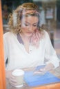 Woman using cell phone in cafe seen through window Royalty Free Stock Photo