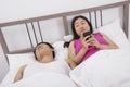 Woman using cell phone while looking at man sleeping in bed Royalty Free Stock Photo