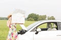 Woman using cell phone while reading map by broken down car at countryside Royalty Free Stock Photo