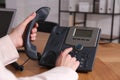 Woman using desktop telephone at wooden table in office, closeup. Hotline service Royalty Free Stock Photo