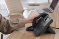 Woman using desktop telephone at wooden table in office, closeup. Hotline service Royalty Free Stock Photo