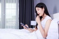Woman using earphone device on mobile phone on bed in bedroom Royalty Free Stock Photo