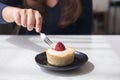 A woman using fork to cutting strawberry cheese tart on white vintage wooden table in cafe
