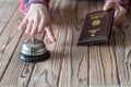 Woman using Germany passport for registration in the hotel. Silver vintage bell on wooden rustic reception desk. Hotel service. Royalty Free Stock Photo