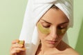 Woman using grapeseed-based eye patches on pastel green background. Natural sustainable skincare