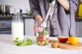 Woman using hand blender to make smoothies. Grey kitchen interior design. Vegetarian, clean eating lifestyle concept Royalty Free Stock Photo