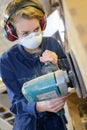 woman using heavy electrical sander and wearing protective equipment