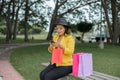 Woman using her cell phone sitting on a garden bench with different colored shopping bags. Royalty Free Stock Photo