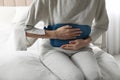 Woman using hot water bottle to relieve abdominal pain on bed at home, closeup Royalty Free Stock Photo