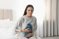 Woman using hot water bottle to relieve abdominal pain on bed at home Royalty Free Stock Photo
