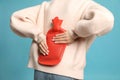 Woman using hot water bottle to relieve back pain on light blue background, closeup Royalty Free Stock Photo