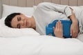 Woman using hot water bottle to relieve menstrual pain on bed at home Royalty Free Stock Photo