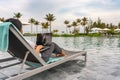 Woman using laptop at swimming pool with beautiful beach view Royalty Free Stock Photo