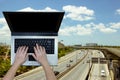 Woman using laptop with blurry expressway background