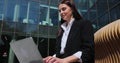 Woman using laptop computer sitting on bench outside modern office building. Woman working on laptop at outdoors. Royalty Free Stock Photo