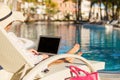 Woman using laptop computer by the swimming pool