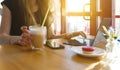 Woman using laptop with cup of coffee, glass of latte, the sun`s rays from the window Royalty Free Stock Photo