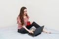 Woman using laptop and drining tea on her bed at home