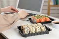 Woman using laptop in office, focus on tasty sushi rolls. Lunch break at work Royalty Free Stock Photo