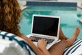 Woman using laptop while relaxing on a sun lounger near swimming pool at the backyard of home Royalty Free Stock Photo