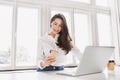 Woman using laptop and smartphone in office. Beautiful girl texting on phone.