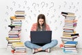 Woman using Laptop. Student Girl working on Computer Search in Internet around Stacks of Books. Question Marks Drawn On White Wall Royalty Free Stock Photo