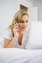 Woman using laptop while talking on mobile phone in bed Royalty Free Stock Photo