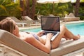 Woman Using Laptop Whilst Relaxing On Sun Lounger By Pool Royalty Free Stock Photo