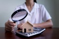 Woman using a magnifying glass to house model and calculator. Searching housing and home insurance concept
